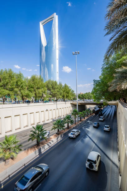 Elevated view from overpass of cars and trucks on multi-lane thoroughfare with landmark architecture in background, clouds reflected in skyscraper facade.