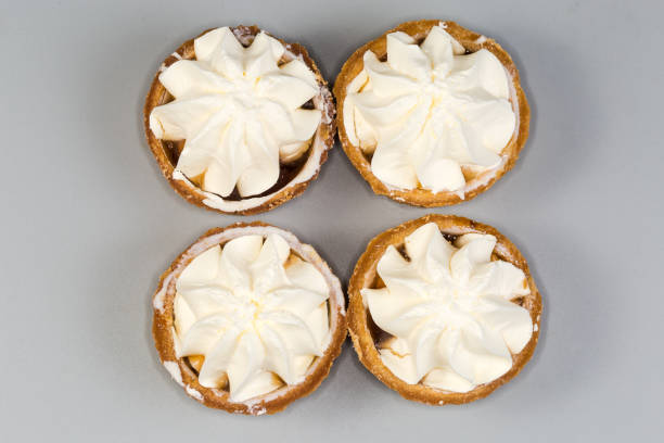 Small tarts, so-called tartlets made with baked shortcrust pastry molds, caramelized pear filling and custard on top on a gray background, top view