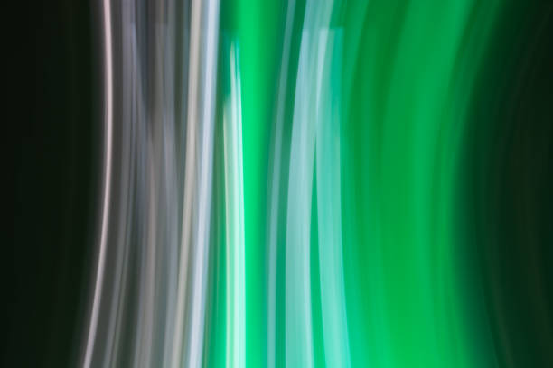 An abstract image featuring vertical streaks of light in shades of green, white, and black. The light trails create a sense of motion and fluidity, reminiscent of lights captured in motion photography