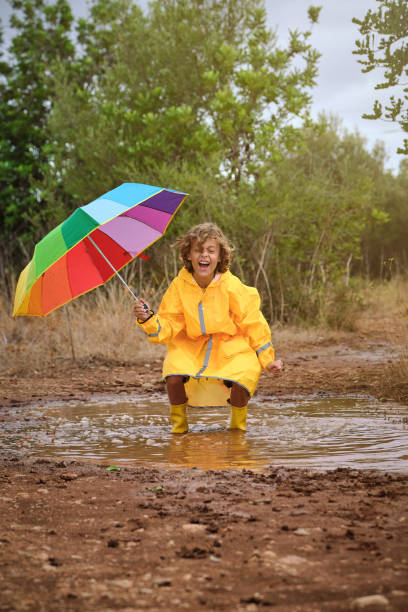 istock Cheerful boy with umbrella jumping in puddle 2152930081