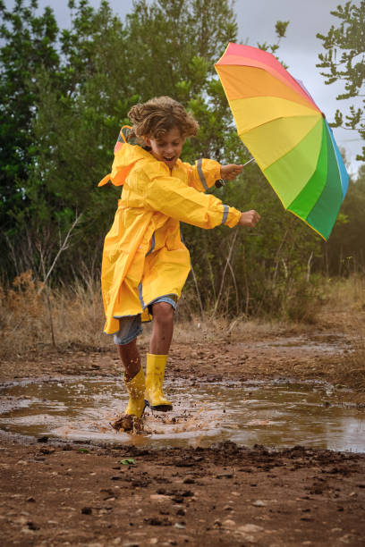 istock Cheerful boy with rainbow umbrella playing in puddle 2152930094