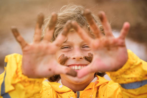 Carefree child with muddy marks on face wearing yellow raincoat looking at camera during rainy autumn day