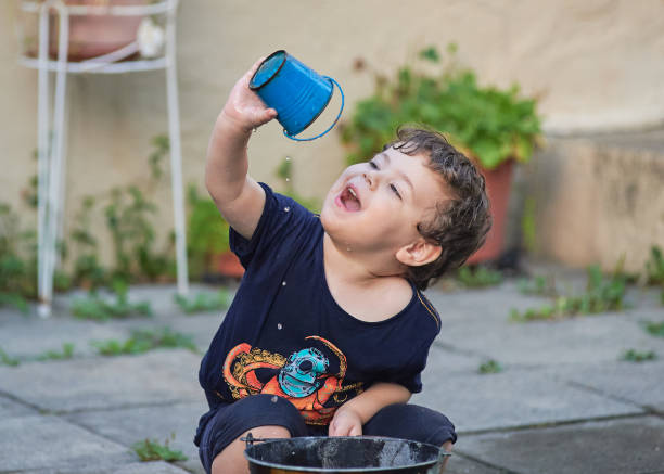young boy playing with a watering hose  and buckets in the backyard