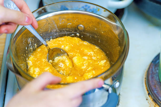 Hands stirring honey, sugar, and butter over a steam bath with a fork