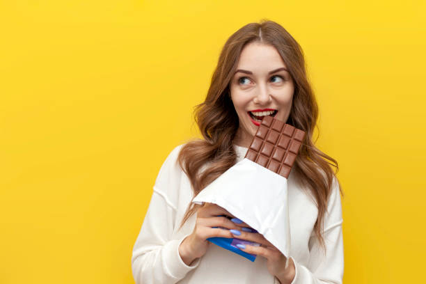 istock young girl eats and bites big chocolate bar and thinks and dreams on yellow isolated background 2152957705