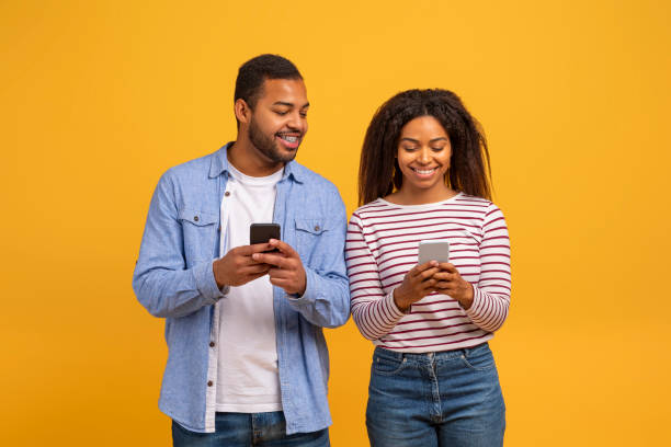 istock Cheerful young black couple using their smartphones against yellow background 2152963751