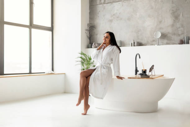 istock Cheerful young eastern woman in bathrobe sitting on bathtub 2152967278