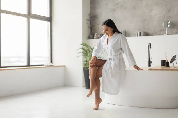 istock Cheerful Young Indian Woman In Bathrobe Touching Smooth Legs 2152967306