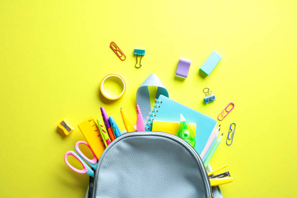 istock Vibrant School Supplies Spill from Backpack - A dynamic flat lay composition featuring a blue backpack overflowing with colorful school essentials against a yellow backdrop. Back to school concept 2152969240