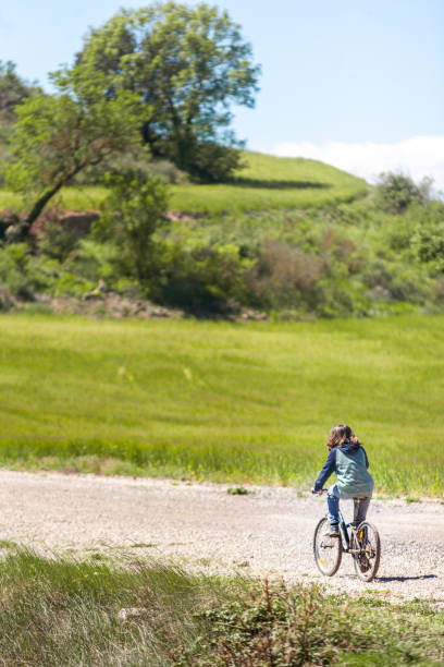 A young boy rides a bicycle down a dirt road in a grassy field. The scene is peaceful and serene, with the boy enjoying the fresh air and the beauty of nature