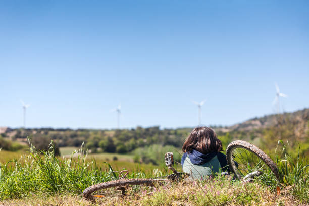 A person is laying on the ground next to a bicycle. The sky is blue and there are wind turbines in the background