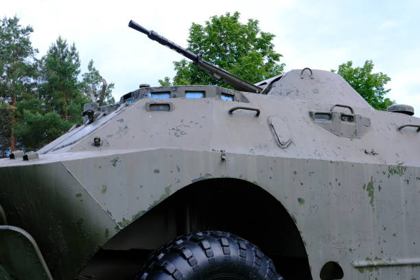 Side view of a military armored vehicle featuring mounted tools such as a shovel, pickaxe, coiled cable, and a warning beacon