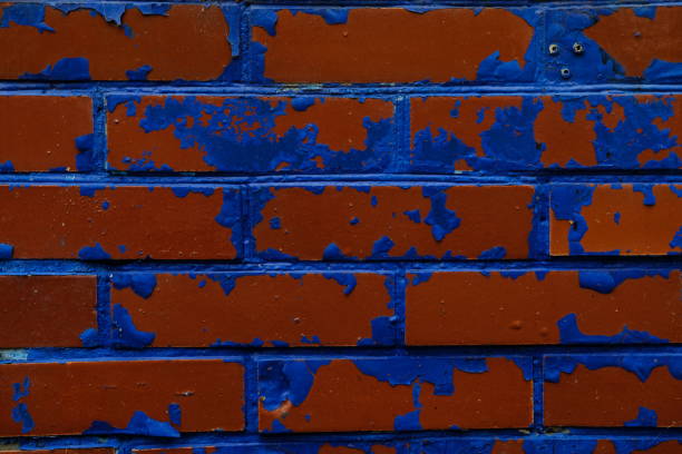 Macro image of an exterior stone wall, with faded and peeled layers of blue, red and white paint in different areas of the surface.