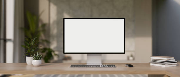 A desktop computer mockup and accessories on a wooden desk in a modern office room.