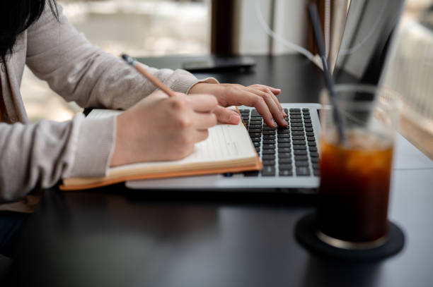 istock A woman working remotely at a coffee shop, taking notes in her notebook while working on her laptop 2152994757
