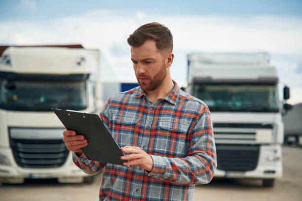 istock Having hard time reading the document in notepad. Man is standing against trucks outdoors 2153010668