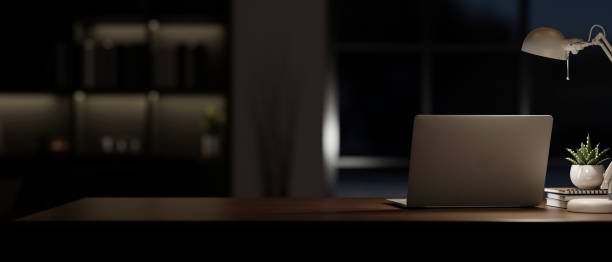 istock A laptop computer on a table in a modern dark room at night with a dim light from a table lamp. 2153012525