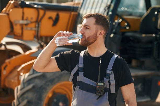 istock Bottle of water, drinking, taking a break. Man is with tractor. Agricultural worker 2153014020