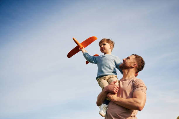 istock Blue sky with white cloud. Father is holding son that playing with toy plane 2153015598