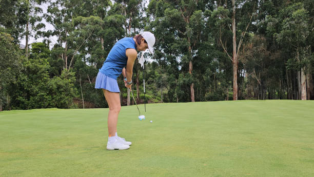 A woman is seen placing a golf ball on the grass while standing on a golf course