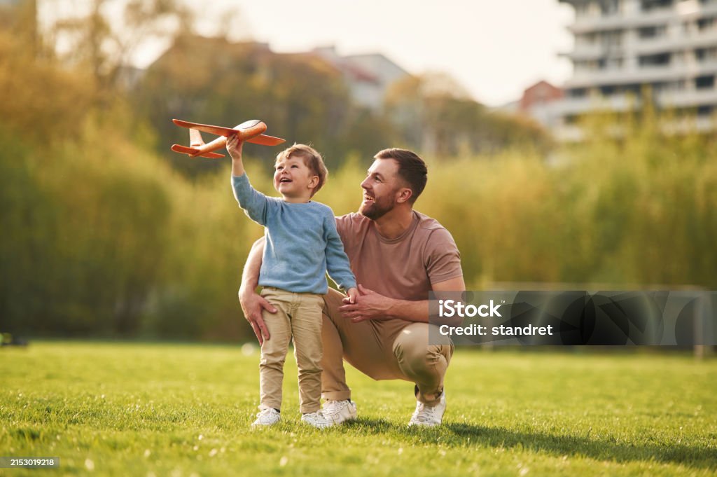 Weekend activities. Playing with toy plane. Happy father with son are having fun on the field at summertime - Royaltyfri Släkt Bildbanksbilder Weekend activities. Playing with toy plane. Happy father with son are having fun on the field at summertime - Royaltyfri Släkt Bildbanksbilder