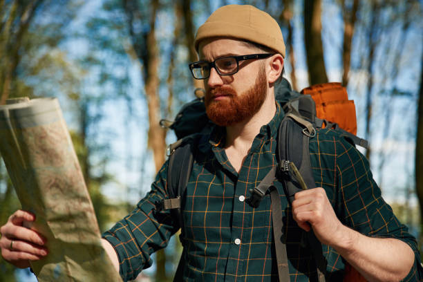 Big paper map. Bearded man is in the forest at daytime