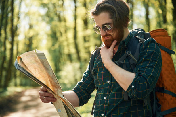 istock Old fashioned paper map in hands. Bearded man is in the forest at daytime 2153022620