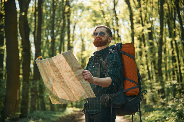 istock Old fashioned paper map in hands. Bearded man is in the forest at daytime 2153022659