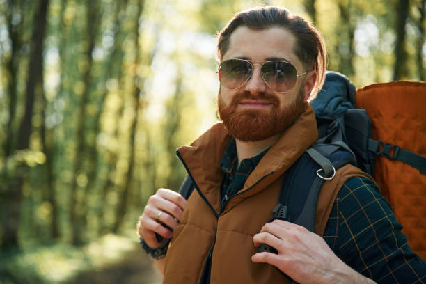In cool sunglasses. Bearded man is in the forest at daytime.