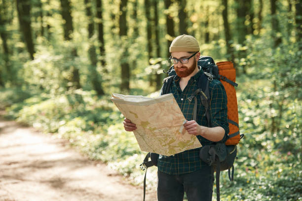 istock Old fashioned paper map in hands. Bearded man is in the forest at daytime 2153023235