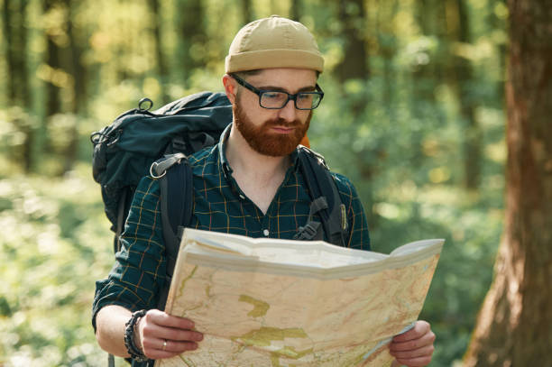 istock Old fashioned paper map in hands. Bearded man is in the forest at daytime 2153023336