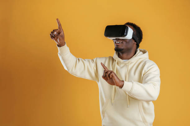 istock Playing VR game. In virtual reality glasses. Black guy is against yellow background 2153028792