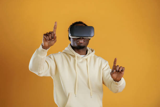 istock Playing VR game. In virtual reality glasses. Black guy is against yellow background 2153028818