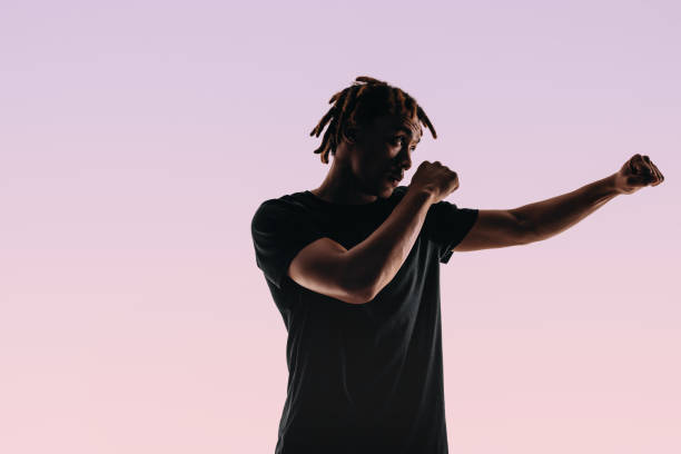 Ft young athlete with dreadlocks practices his boxing skills in a pink sports training studio, demonstrating strength and striking abilities with bare knuckles. This silhouette showcases boxing's intense combat and fitness lifestyle.
