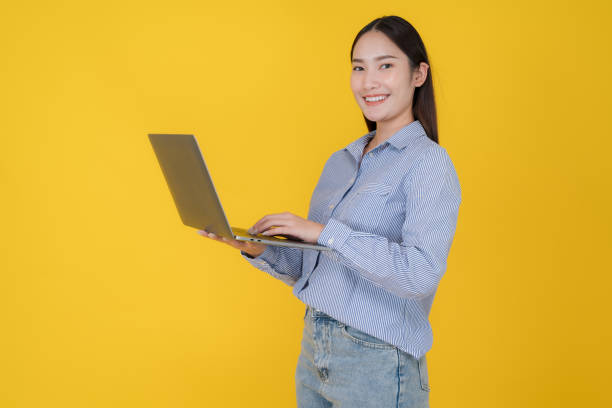 istock Confident young woman with laptop on yellow background 2153032197