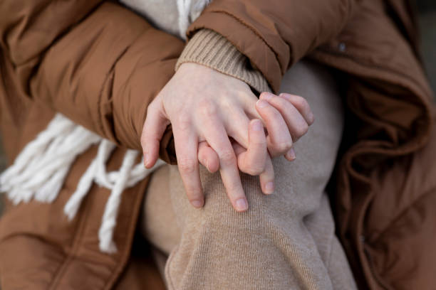 A close-up shot of a pair of unrecognisable hands. The person has their fingers interlaced and is resting their hands on their knee. They are wearing warm clothing, sitting outdoors in Newcastle upon Tyne, North East England.