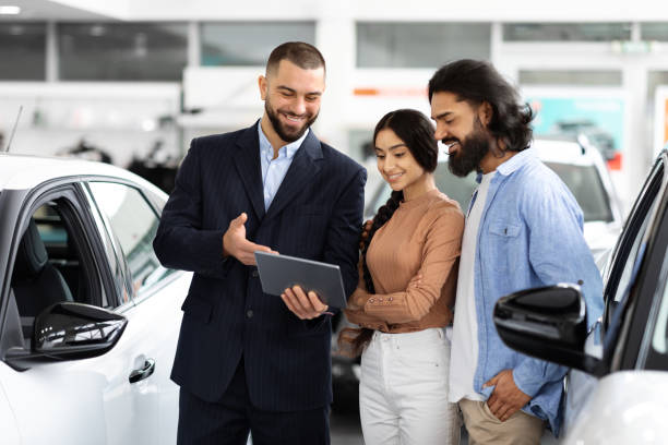 istock Auto dealer with digital tablet explains car features to couple 2153047396