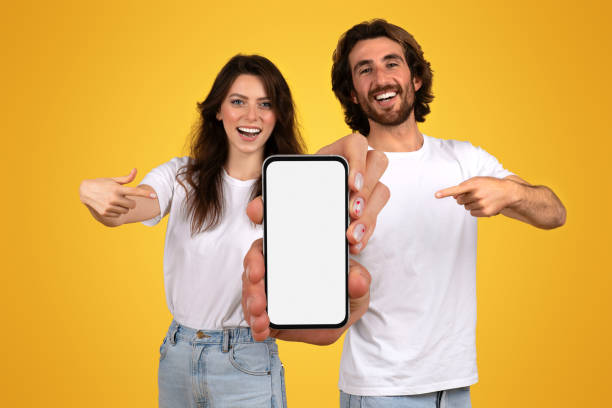 istock Enthusiastic young couple in white t-shirts presenting a smartphone with a blank screen 2153049602