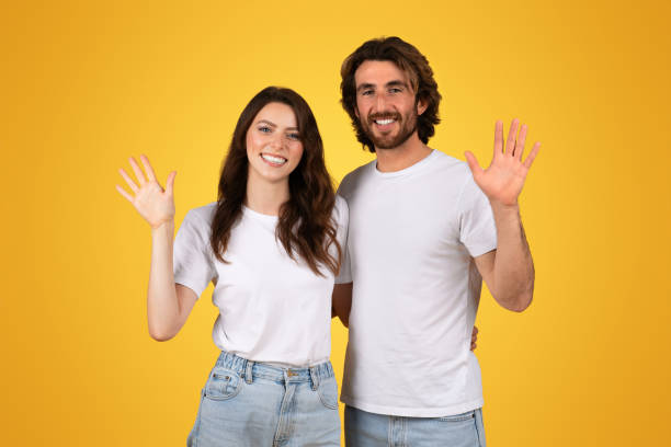 istock Smiling young couple in white shirts waving hello with an open hand gesture 2153049626