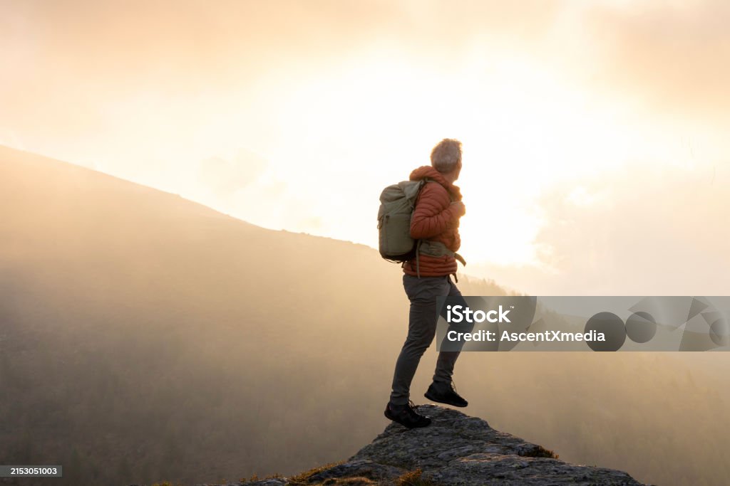 Mature hiker pauses on rock above misty hills - 1人のロイヤリティフリーストックフォト Mature hiker pauses on rock above misty hills - 1人のロイヤリティフリーストックフォト