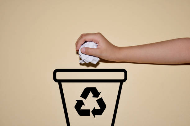 Hand throwing crumpled paper into dustbin with recycling symbol. Recycling concept.