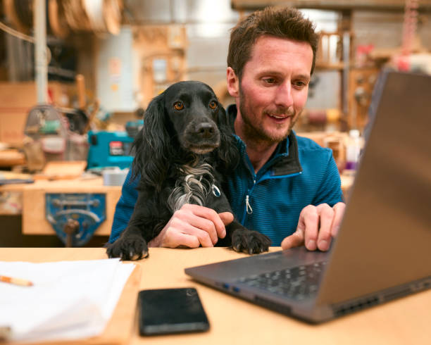 istock Carpenter With Pet Spaniel Working In Woodwork Workshop Using Laptop Together 2153061253