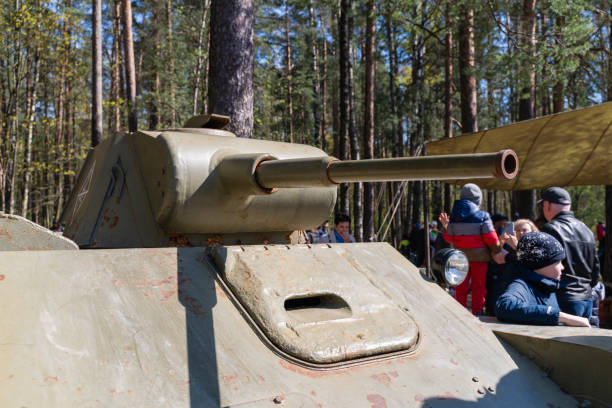 St. Petersburg, Russia, May 9, 2024. The frontal part of a vintage tank from the war with a turret and an artillery mount, armored steel, powerful weapons, a military exhibition in the park, people around, tree trunks, sunny day, rest and entertainment, spring.