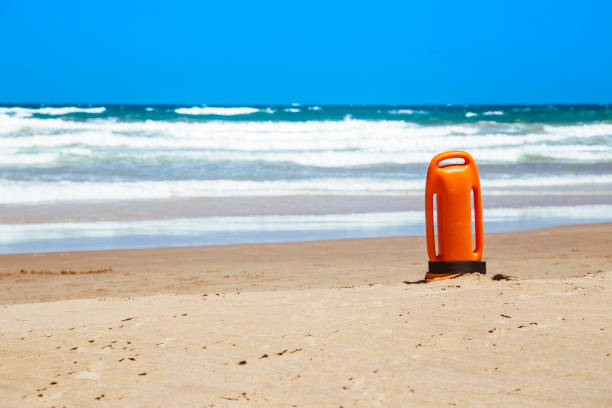 Orange rescue buoy planted on sand beach, in vertical position on the sand. Horizontal composition. Copy space at left.