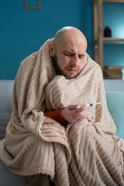 istock Tired sickness man suffering from a high temperature and headache. Sick guy wrapped in blanket with a thermometer in his hand 2153063763