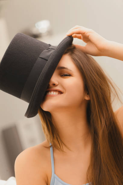 Bright-eyed woman with long hair enjoys a playful moment with a black hat, her joy evident in her radiant smile