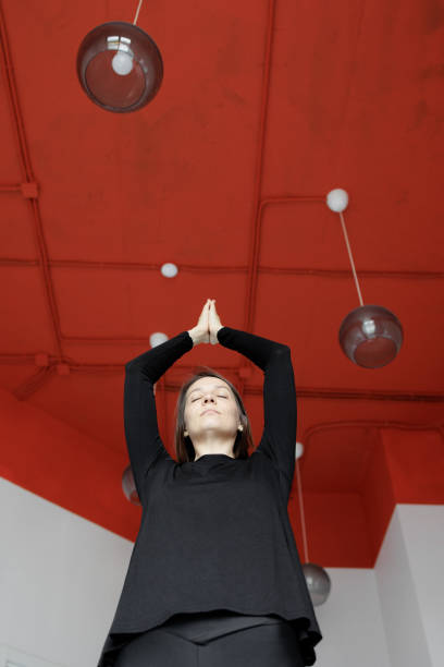 A young hispanic women sits in yoga pose at an indoor studio. She is smiling at the camera and looks relaxed. She is in a group workout.