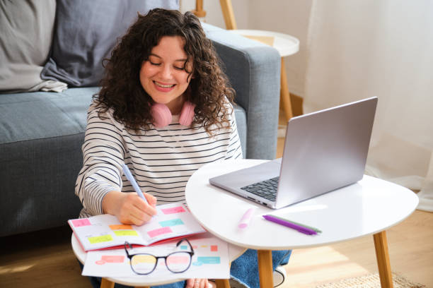istock A woman is sitting on the floor with a laptop and a notebook. 2153086412