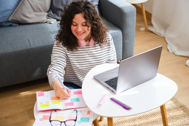 istock A woman is sitting on the floor with a laptop and a notebook. 2153086526