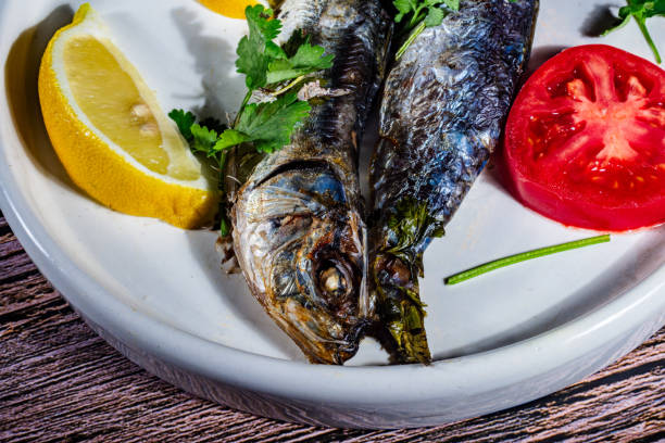 A plate of fish and tomatoes with a lemon wedge on the side